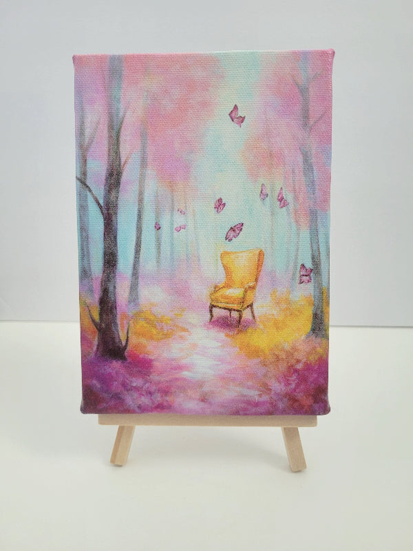 A vertical canvas painting of a whimsical forest scene with a yellow armchair, pink and purple butterflies, and soft blue and pink trees, displayed on a small wooden easel against a plain white background.